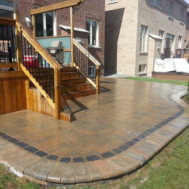 Cedar deck stairs with black metal railings leading to a stamped concrete patio in Durham Region